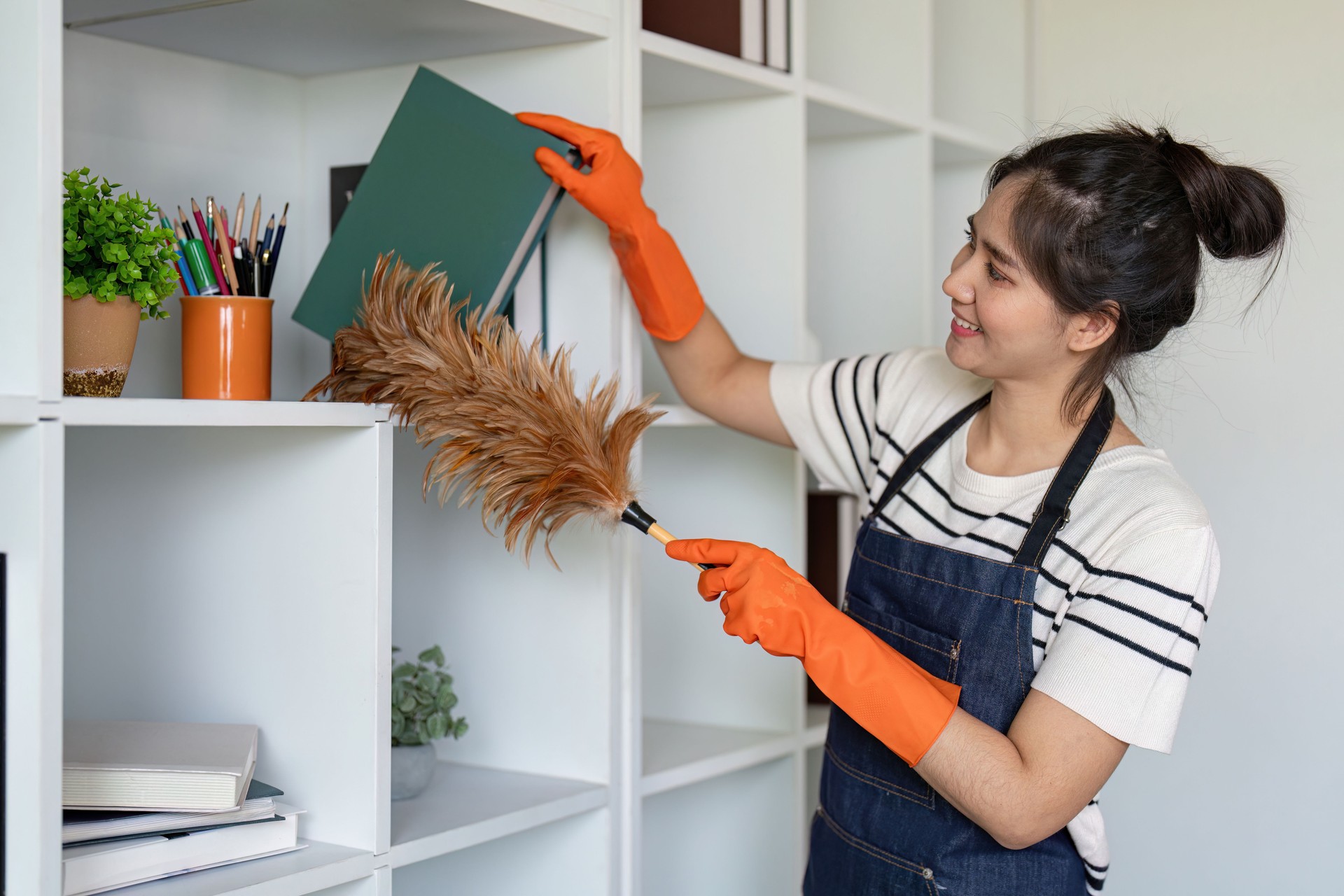 Woman dusting shelves with feather duster in office setting